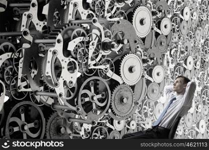 He possesses constructive thinking. Young relaxed businessman sitting in chair and looking at gears mechanism