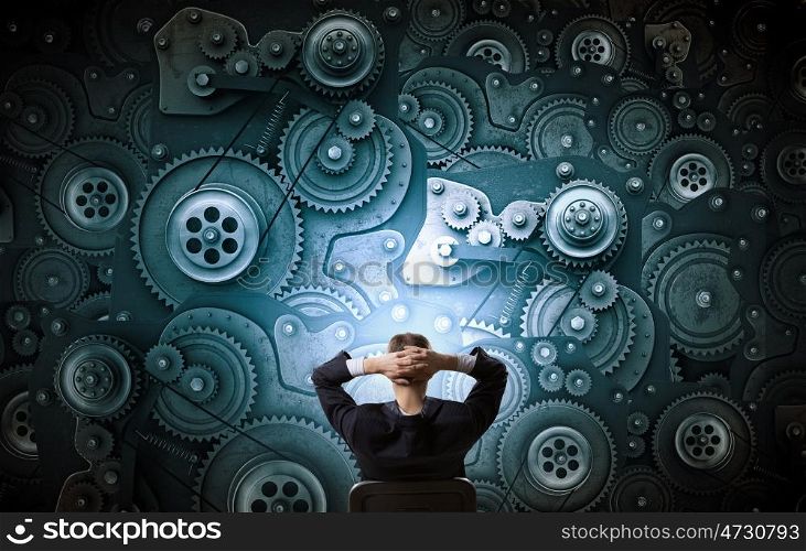 He possesses constructive thinking. Young relaxed businessman sitting in chair and looking at gears mechanism