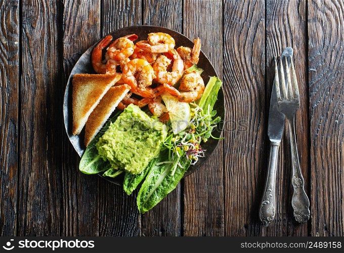 Hea<hy appetizer or snack avocado shrimp bruschetta. Fried shrimp and mashed avocado on black plate. Hea<hy appetizer or snack avocado shrimp bruschetta. Fried shrimp and mashed avocado on plate for breakfast