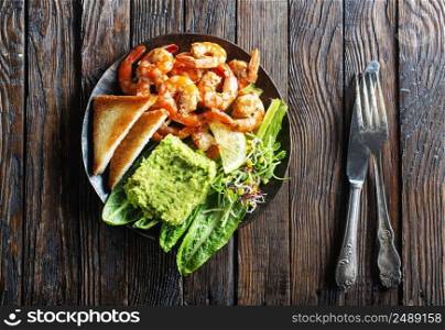 Hea<hy appetizer or snack avocado shrimp bruschetta. Fried shrimp and mashed avocado on black plate. Hea<hy appetizer or snack avocado shrimp bruschetta. Fried shrimp and mashed avocado on plate for breakfast