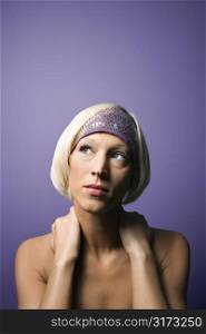 Head and shoulder portrait of bare young adult Caucasian woman on purple background wearing headband.