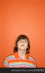 Head and shoulder portrait of Caucasian boy looking up standing against orange background.