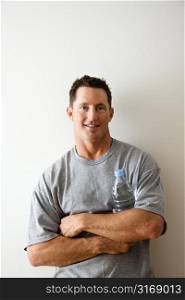 Head and shoulder portrait of man in t-shirt against white wall holding water bottle and smiling.