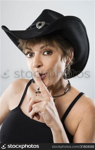 Head and shoulder portrait of pretty Caucasian woman wearing cowboy hat holding finger to mouth.