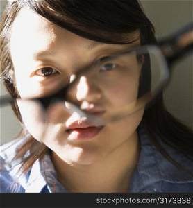 Head and shoulder portrait of pretty young Asian woman holding eyeglasses.