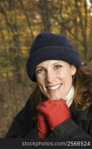 Head and shoulder portrait of smiling Caucasian woman in hat and gloves in woods.