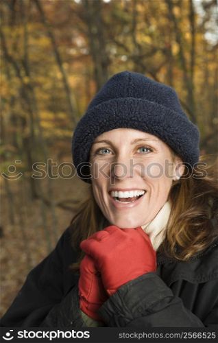 Head and shoulder portrait of smiling Caucasian woman in hat and gloves in woods.