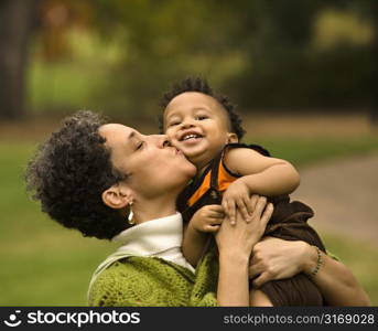Head and shoulder portrait of woman holding and kissing boy as he smiles.