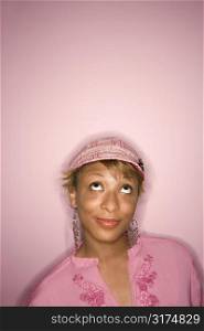 Head and shoulder portrait of young African-American adult woman on pink background looking up with eyes.