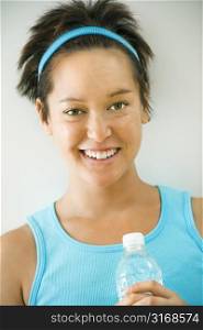 Head and shoulder portrait of young woman in fitness wear holding bottled water and smiling.