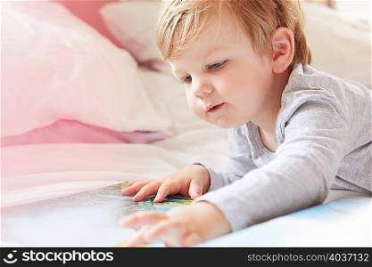 Head and shoulders of boy on bed lying on front looking at storybook