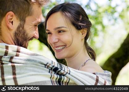 Head and shoulders of young couple wrapped in blanket face to face smiling
