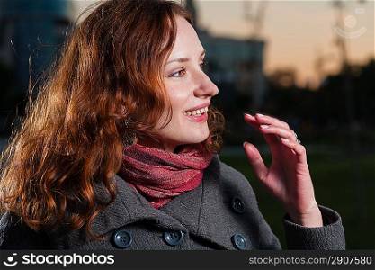 Head and shoulders portrait in profile of the smiling redhead 20s women outdoor in autumn park, weared scarf and coat