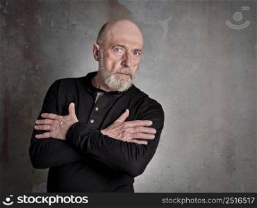 Head and shoulders portrait of a bald, bearded, thoughtful senior man in a black shirt