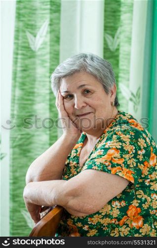 Head and shoulders portrait of a happy smiling senior woman resting her chin on her hands and looking directly at the camera