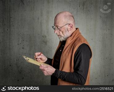 Head and shoulders portrait of a senior, bald and bearded man writing notes and sketching on a clipboard