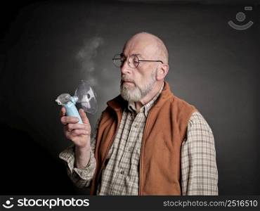 Head and shoulders portrait of a senior man using a portable handheld nebulizer, self care and respiratory therapy concept