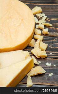 Head of parmesan or parmigiano hard cheese and pieces on wooden background or table. Head of parmesan or parmigiano hard cheese and pieces on wooden background