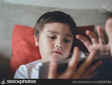 Head shot appy kid watching cartoon on tablet, Candid shot cute boy playing game online with friends on internet, A Child sitting on sofa relaxing at home on weekend