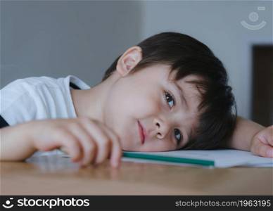 Head shot cute boy looking at camera with smiling face while playing with colour pencil, Preschool child boy laying head down on table relaxing after finished school homework,Education concept