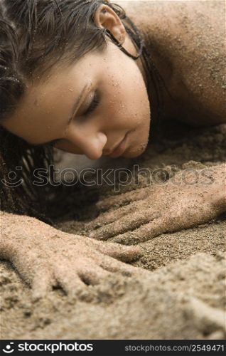 Head shot of Caucasian young adult nude woman lying in sand.