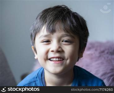 Head shot of healthy kid, Portrait happy child looking at camera with smiling face, candid shot cute little boy relaxing at home. Positive children concept