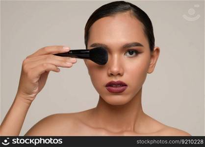 Head shot Portrait, Beauty portrait of asian attractive sensual young woman pose holding makeup blusher brush close her eye, isolated over gray background, copy space