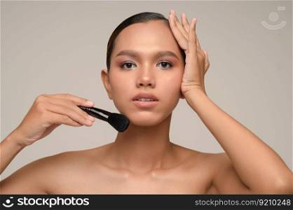 Head shot Portrait, Beauty portrait of asian attractive sensual young woman pose holding makeup blusher brush isolated over gray background, copy space