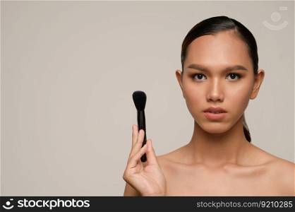 Head shot Portrait, Beauty portrait of asian attractive sensual young woman pose holding makeup blusher brush isolated over gray background, copy space