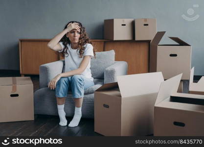 Headache from moving. Exhausted woman sitting among packed cardboard boxes. Spanish young lady in jeans and white t-shirt going to relocate. Depression and stress from moving concept.. Headache from moving. Exhausted spanish woman sitting among packed cardboard boxes.