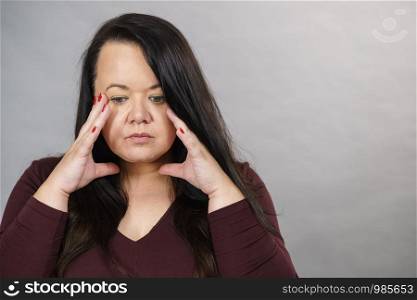 Headache, migraine and stress. Worried plus size adult upset woman suffering from head pain, studio shot on gray.. Worried woman having painfull headache