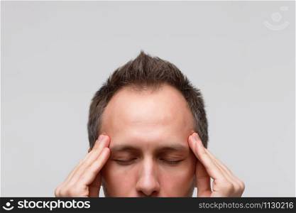 Headache, nervous tension concept. Close up portrait of man tries to concentrate, gather with thoughts, meditating and massaging his temples, closed eye, isolated on gray background. Strong migraine