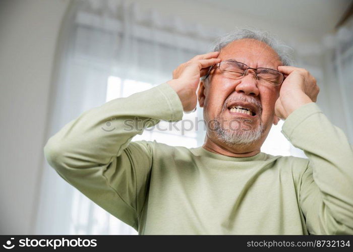 Headache. Sad Asian senior man chronic migraine pain massaging, old man holds head with hand for headache disease in living room at home, Old age health problems, healthcare