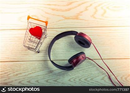 Headphones and a shopping trolley with a red heart in it on wooden background