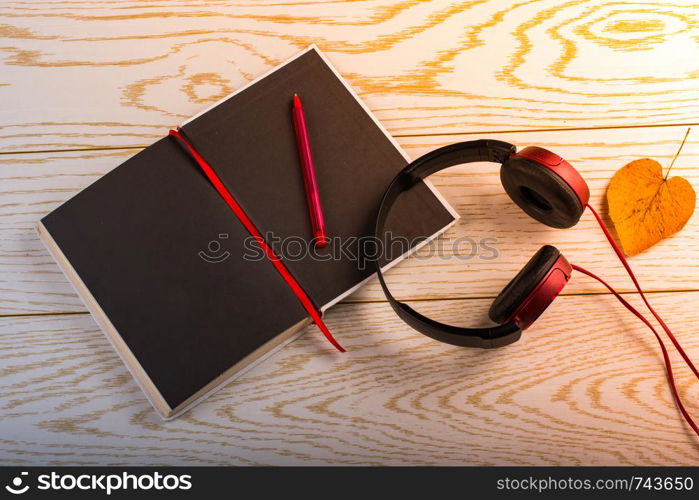 Headphones, notebook, pen and leaf heart on a wooden background