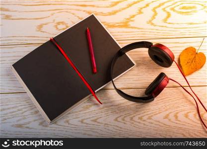 Headphones, notebook, pen and leaf heart on a wooden background