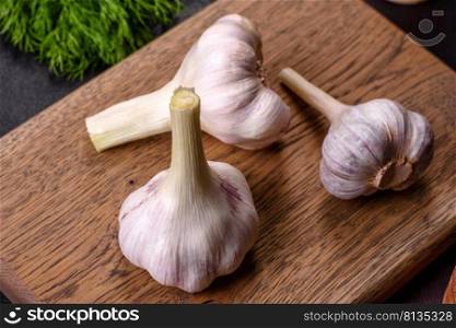 Heads of fresh white garlic on a wooden cutting board against a dark concrete background. Cooking at home. Heads of fresh white garlic on a wooden cutting board