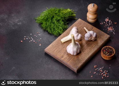 Heads of fresh white garlic on a wooden cutting board against a dark concrete background. Cooking at home. Heads of fresh white garlic on a wooden cutting board