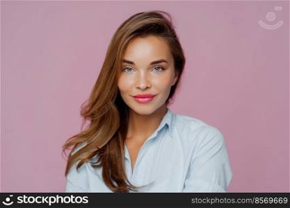 Headshot of lovely European lady has blue eyes, red painted lips, healthy skin, long hair, looks directly at camera, wears shirt, poses over purple background. Beautiful woman ready for job interview