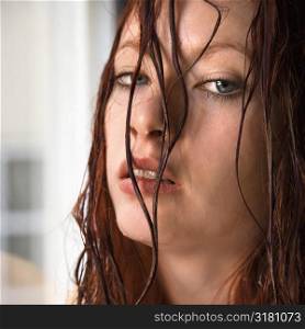 Headshot of pretty young redhead woman with wet hair hanging in face making eye contact.