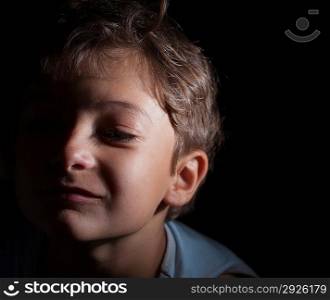 headshot of the boy in the dark, focused light on the one side, sad alone 7 years old