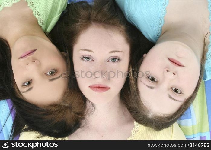 Headshot of three young teen girls laying side by side with serious or bored expressions on faces.