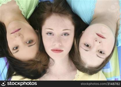 Headshot of three young teen girls laying side by side with serious or bored expressions on faces.