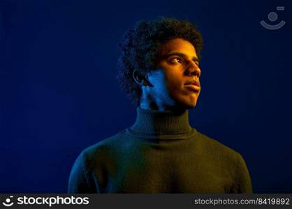 Headshot of young serious man with pensive facial expression looking away over dark studio background. Young serious man looking away over dark studio background