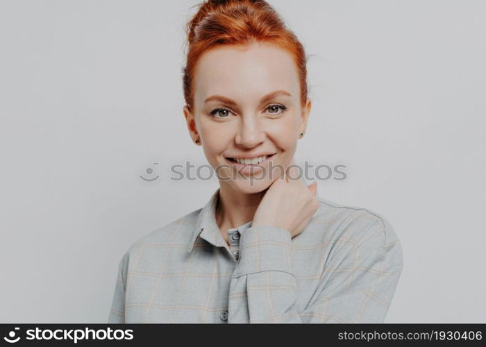 Headshot portrait of happy redhead woman looking at camera white toothy smile, positive millennial red haired female 30s posing isolated over grey studio wall background, dressed in casual shirt. Happy redhead woman looking at camera white toothy smile isolated over grey background