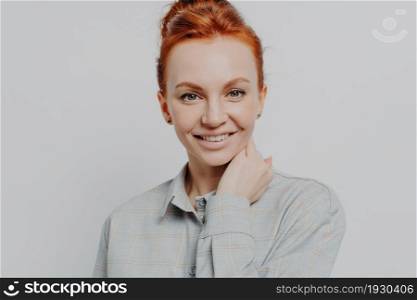 Headshot portrait of happy redhead woman looking at camera white toothy smile, positive millennial red haired female 30s posing isolated over grey studio wall background, dressed in casual shirt. Happy redhead woman looking at camera white toothy smile isolated over grey background
