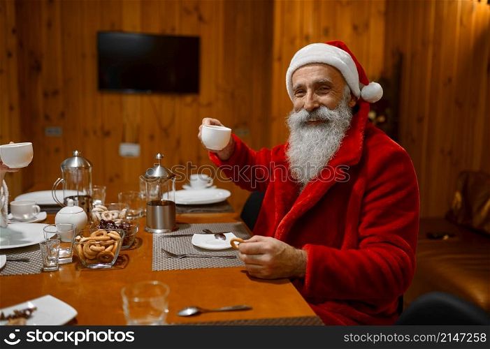Headshot portrait of happy smiling Santa Claus drinking tea and eating bagels in sauna rest room. Portrait of happy smiling Santa drinking tea