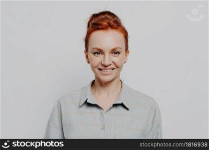 Headshot portrait of happy young caucasian ginger woman being satisfied and feeling happy, looking at camera cheerful while standing isolated on grey background. Positive emotions concept. Headshot portrait of happy young caucasian ginger woman being satisfied and feeling happy