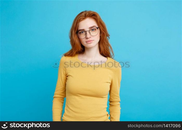 Headshot Portrait of tender redhead teenage girl with serious expression looking at camera. Caucasian woman model with ginger hair posing indoors.Pastel blue background. Copy Space.
