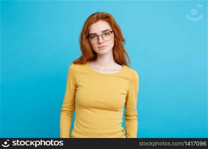 Headshot Portrait of tender redhead teenage girl with serious expression looking at camera. Caucasian woman model with ginger hair posing indoors.Pastel blue background. Copy Space.